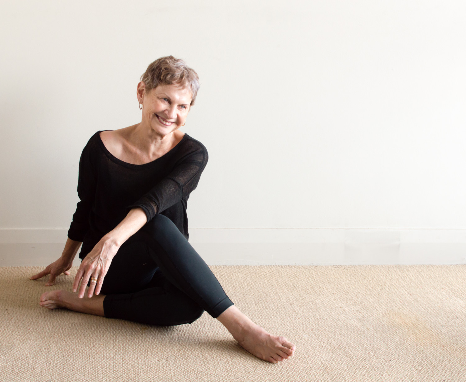 Older woman in black yoga clothing laughing in relaxed seated yoga
