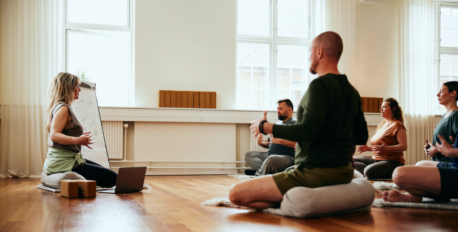 Female yoga instructor doing breathing exercises to students while sitting on the floor of a studio during a class
