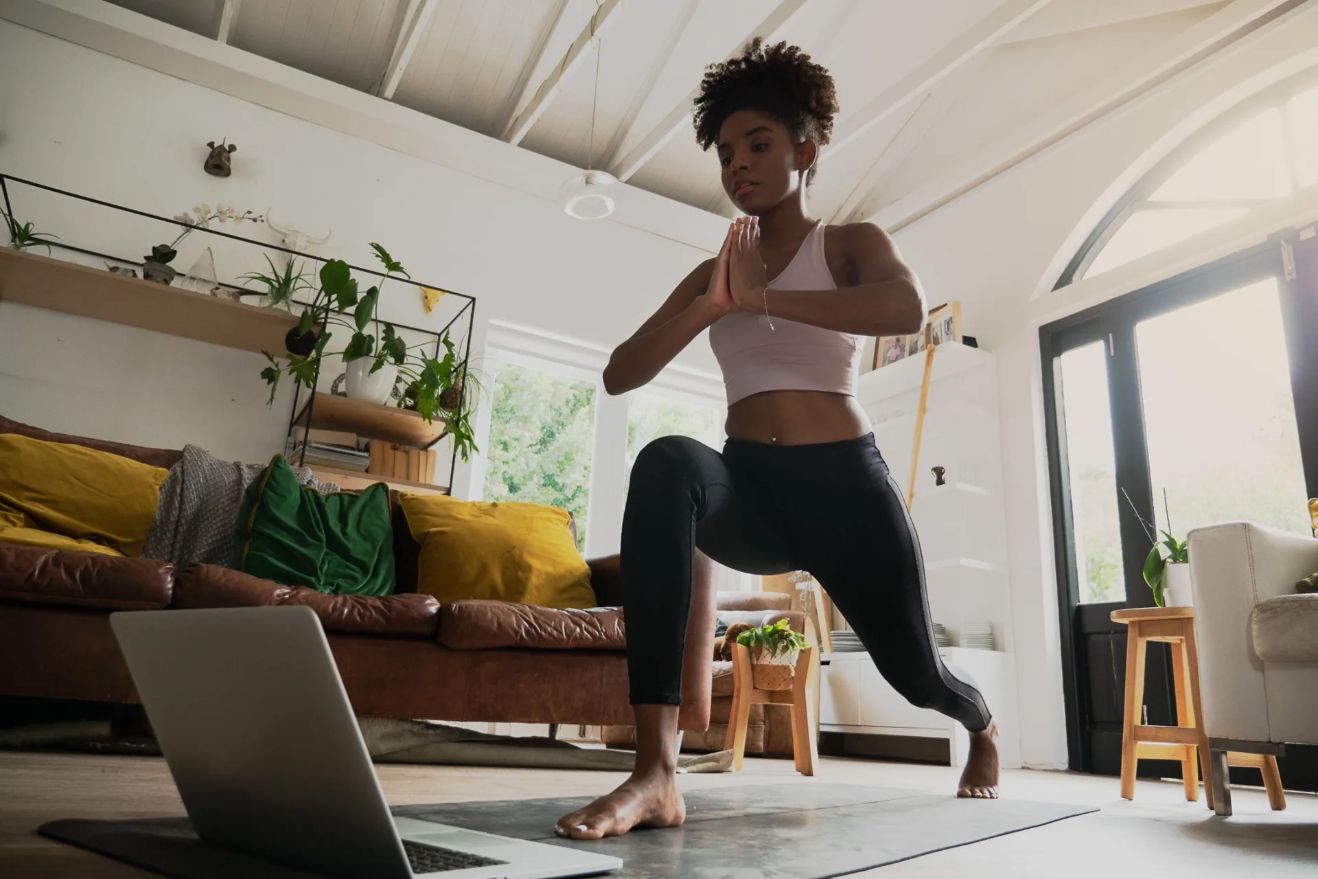 Woman practicing a yoga lunge at home beside a laptop